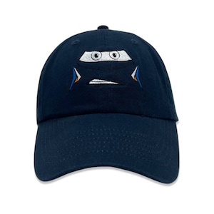 May include: A navy blue baseball cap with an embroidered image of a cartoon car with a face. The car is white with blue and orange accents.