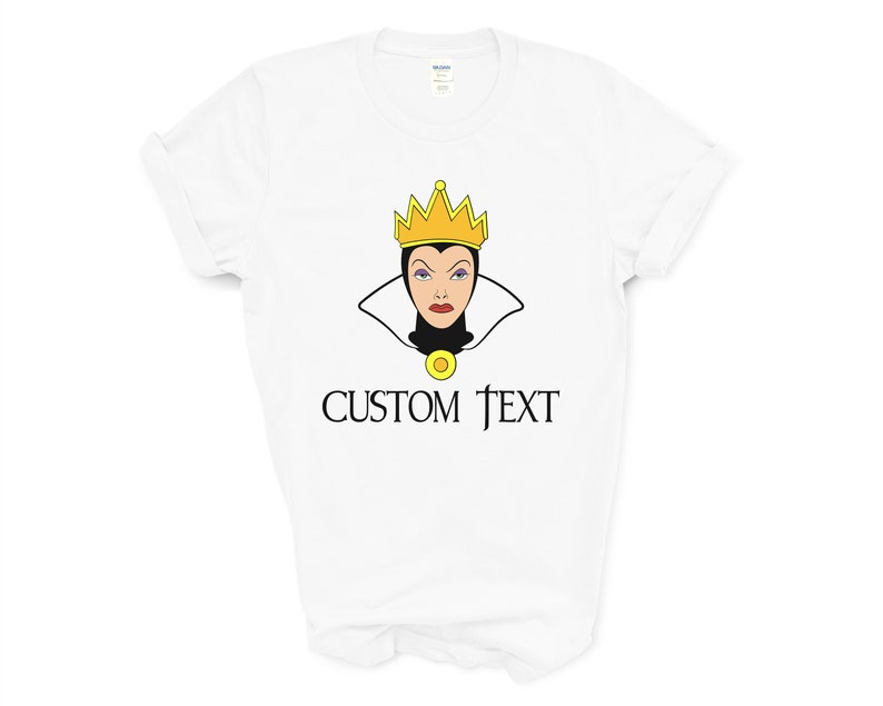 以下が含まれることがあります： 白いTシャツに、金色の冠と白黒の襟をつけた白雪姫の悪の女王の漫画の画像がプリントされています。画像の下には「CUSTOM TEXT」という文字が印刷されています。