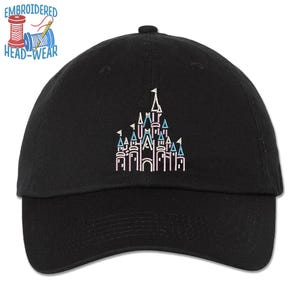 Pode incluir: Bon&eacute; de beisebol preto com um contorno bordado do castelo da Cinderela em rosa, azul e branco. O texto "EMBROIDERED HEAD-WEAR" est&aacute; acima do castelo.