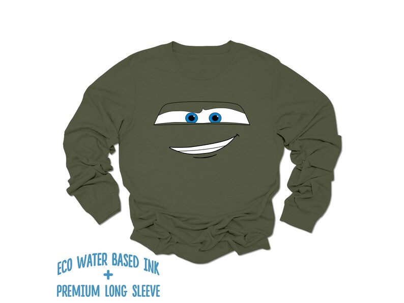 May include: A green long-sleeve shirt with a cartoon face printed on the front. The face has blue eyes and a white smile.
