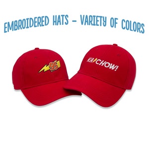 May include: Two red baseball caps with embroidered designs. One cap features a yellow lightning bolt and the number 95. The other cap has the text "KACHOW!" embroidered in white.