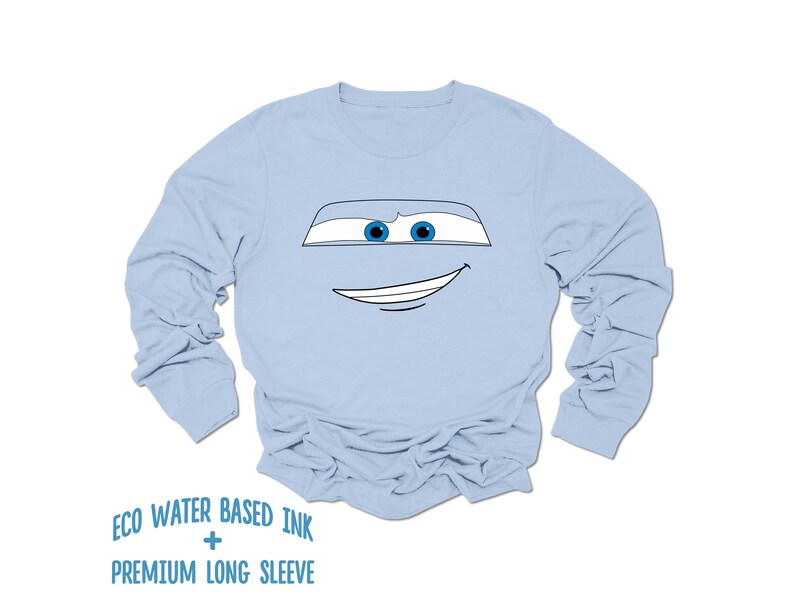 May include: Light blue long-sleeved t-shirt with a cartoon face of a car with blue eyes and a white outline. The text "ECO WATER BASED INK + PREMIUM LONG SLEEVE" is printed below the image.