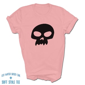 Pu&ograve; includere: Una maglietta rosa con una grafica di teschio nero. Il testo "ECO WATER BASED INK + SOFT STYLE TEE" &egrave; stampato sul fondo della maglietta.