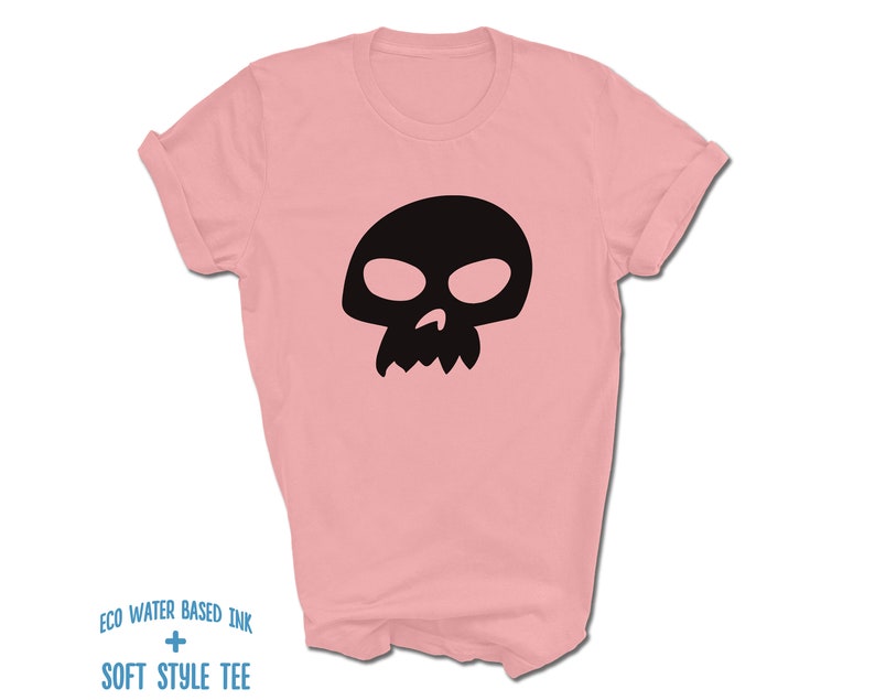 Pu&ograve; includere: Una maglietta rosa con una grafica di teschio nero. Il testo "ECO WATER BASED INK + SOFT STYLE TEE" &egrave; stampato sul fondo della maglietta.