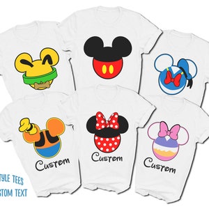May include: Five white t-shirts with different Disney character faces printed on them. The characters are Mickey Mouse, Minnie Mouse, Donald Duck, Goofy, and Pluto. The shirts have the word "Custom" printed on them.