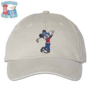 May include: A beige baseball cap with an embroidered image of Mickey Mouse playing golf. The embroidery is in red, blue, and black.