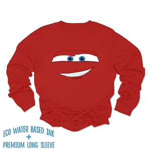 May include: Red long-sleeve shirt with a cartoon face of a red race car with blue eyes and a smile. The shirt has the text "ECO WATER BASED INK + PREMIUM LONG SLEEVE" printed on the bottom.