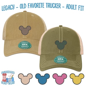 May include: Two trucker hats with a Mickey Mouse silhouette embroidered on the front. The hats are brown and green with a mesh back. The text "LEGACY - OLD FAVORITE TRUCKER - ADULT FIT" is at the top of the image. The text "EMBROIDERED HEAD-WEAR" is at the bottom of the image. The text "LEGACY OFA" is on a green label on each hat.