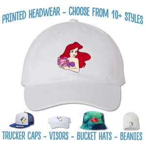 May include: A white baseball cap with a printed image of Ariel from The Little Mermaid. The image shows Ariel holding a seashell. The text "PRINTED HEADWEAR - CHOOSE FROM 10+ STYLES" is at the top of the image. The text "TRUCKER CAPS - VISORS - BUCKET HATS - BEANIES" is at the bottom of the image.