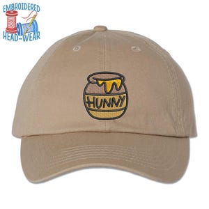 May include: A beige baseball cap with an embroidered image of a honey pot with the word "Hunny" on it.