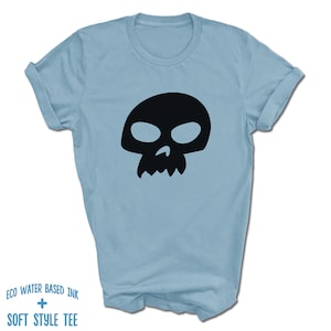 Pu&ograve; includere: Una t-shirt blu chiaro con una grafica di teschio nero. Il testo "ECO WATER BASED INK + SOFT STYLE TEE" &egrave; stampato sul fondo della t-shirt.