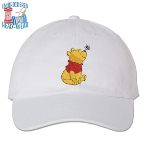 May include: White baseball cap with an embroidered image of Winnie the Pooh sitting and looking at a bee.