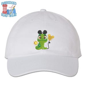 May include: White baseball cap with an embroidered design of a green chameleon wearing Mickey Mouse ears and holding a yellow balloon. The sun is also embroidered on the cap. The text "EMBROIDERED HEAD-WEAR" is above the cap.