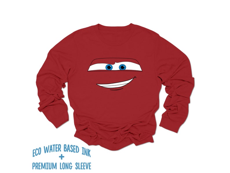 May include: Red long-sleeve shirt with a cartoon face of a red race car with blue eyes and a smile. The shirt has the text "ECO WATER BASED INK + PREMIUM LONG SLEEVE" printed on the bottom.