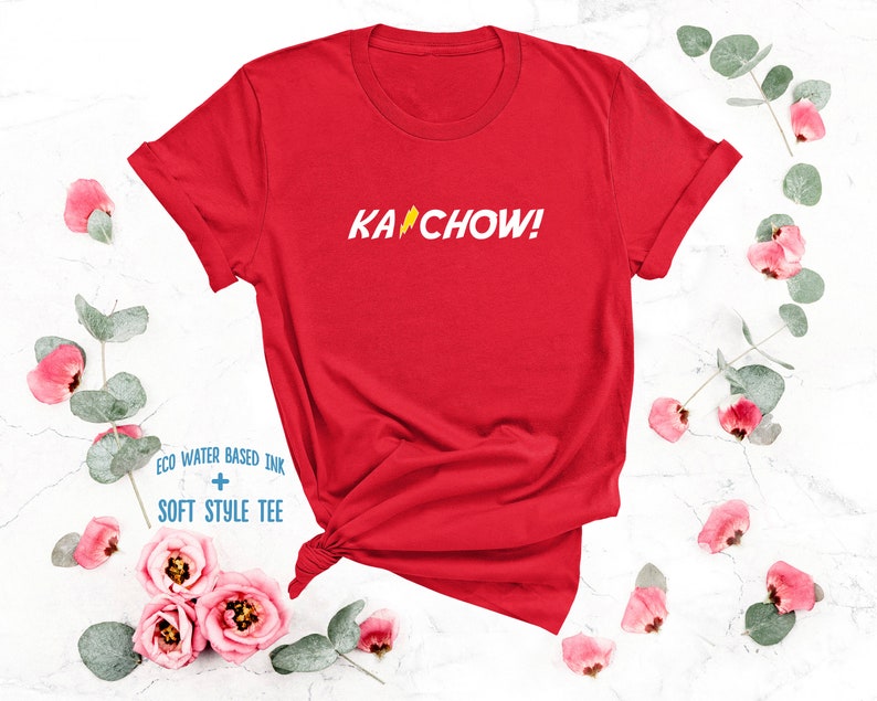 Op de afbeelding: Rood T-shirt met een witte bliksem en de tekst "KACHOW!" gedrukt op de voorkant. Het shirt is gemaakt met milieuvriendelijke, watergebaseerde inkt en een zachte stijl.