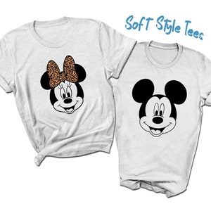 May include: Two white t-shirts with a black and white Mickey Mouse and a Minnie Mouse design. Minnie Mouse has a brown and black leopard print bow.