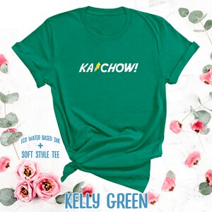 Op de afbeelding: Een kellygroen T-shirt met de tekst "KACHOW!" in geel met een bliksem-graphic. Het shirt is gemaakt met eco-water gebaseerde inkt en een zachte stijl tee.