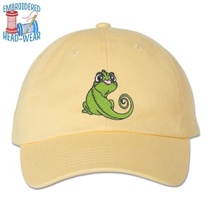 May include: A yellow baseball cap with an embroidered green chameleon design. The chameleon has a pink tongue sticking out and is wearing glasses.