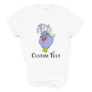 May include: White t-shirt with a purple cartoon image of Ursula from The Little Mermaid. The text "CUSTOM TEXT" is printed below the image.