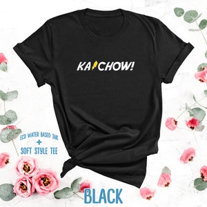 Op de afbeelding: Zwart T-shirt met een gele bliksem en de tekst "KACHOW!" gedrukt op de voorkant.