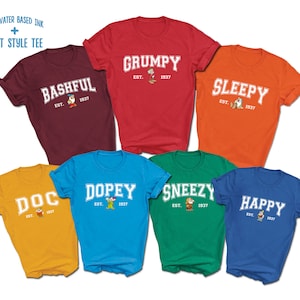 May include: Seven different colored t-shirts with a white graphic print of a Disney character and the text "EST. 1937". The characters are: Bashful, Grumpy, Sleepy, Doc, Dopey, Sneezy, and Happy.