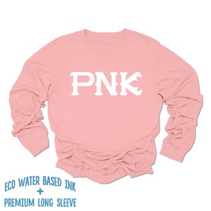 May include: A pink long-sleeved t-shirt with the letters "PNK" printed in white on the front. The shirt is made with eco-friendly water-based ink and is described as "premium long sleeve".
