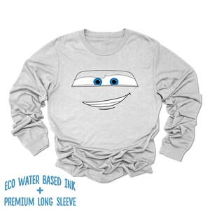 May include: A gray long-sleeve t-shirt with a black and white outline of a cartoon face with blue eyes. The text "ECO WATER BASED INK + PREMIUM LONG SLEEVE" is printed below the image.