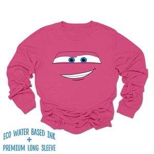 May include: Pink long-sleeved shirt with a cartoon face of a red car with blue eyes and a smile. The shirt has the text "ECO WATER BASED INK + PREMIUM LONG SLEEVE" printed on the bottom.
