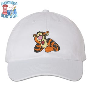 May include: White baseball cap with an embroidered image of a cartoon tiger with orange and black stripes. The tiger is smiling and has a pink nose.