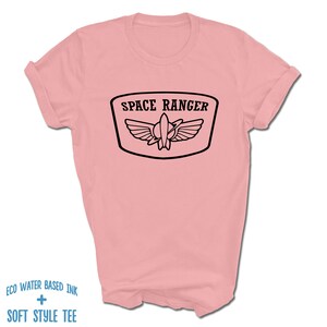 May include: A pink t-shirt with a black graphic of a space ranger badge with the text "SPACE RANGER".