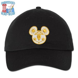 May include: Black baseball cap with a yellow and white embroidered design of a stylized mouse head. The mouse head has sun-like shapes for ears and a building-like shape in the center. The text "EMBROIDERED HEAD-WEAR" is above the cap.