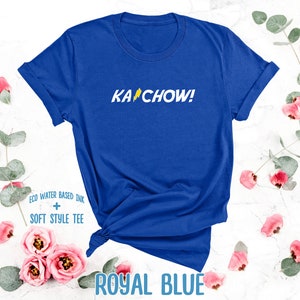 Op de afbeelding: Een koninklijk blauw T-shirt met de tekst "KACHOW!" in geel met een bliksem-afbeelding. Het T-shirt is gemaakt met milieuvriendelijke, watergebaseerde inkt en een zachte stijl.