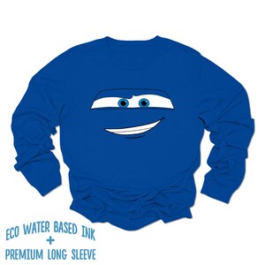 May include: A royal blue long-sleeved shirt with a cartoon face of a car with blue eyes and a white smile.