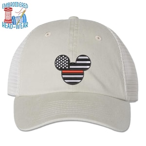 May include: A white trucker hat with a black and red embroidered Mickey Mouse head with an American flag design. The hat has a mesh back.