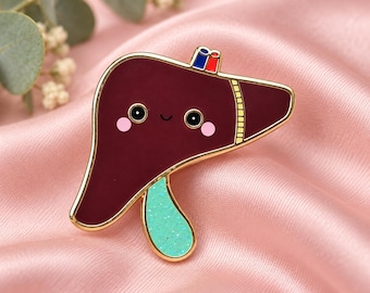 Puede incluir: Un pin de esmalte con borde dorado en forma de hígado, con cuerpo color granate oscuro, cara sonriente con mejillas rosadas, vesícula biliar verde menta brillante y un pequeño detalle rectangular azul y rojo en la parte superior, perfilado en oro.