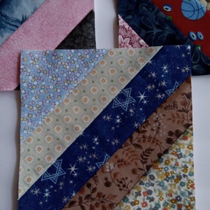 May include: A patchwork quilt block with five different fabric strips sewn together in a diagonal pattern. The fabrics are a light blue with white flowers, a beige with white daisies, a dark blue with white stars, a brown with a floral pattern, and a light blue with small red and yellow flowers.