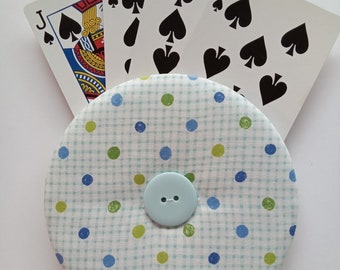 May include: A blue and white polka dot fabric covered button with a light blue button in the center.  The button is surrounded by playing cards, including the Jack, 8, 9, and 10 of spades.