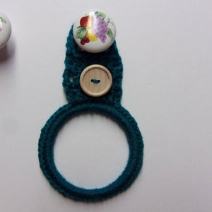 May include: Teal crocheted pot holder with a wooden button and a white ceramic button with a floral design.