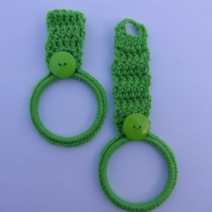 May include: Two green crocheted dish towels with green buttons. The towels are hanging on a white background.