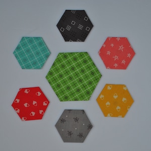 May include: Six hexagon-shaped fabric patches with different patterns. The patches are in shades of green, red, yellow, blue, gray, and black. The patterns include stars, acorns, leaves, and geometric shapes.