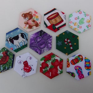 May include: Nine colorful hexagon-shaped fabric patches with various designs, including a bear, a cow, an owl, a candy cane, a frog, strawberries, flip-flops, a ladybug, and a drum.