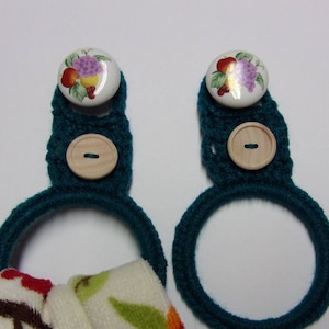 May include: Two teal crocheted towel rings with wooden buttons and ceramic buttons with fruit and floral designs.