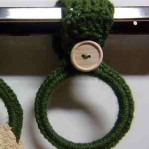 May include: Two green crocheted towel rings with wooden buttons. The rings are hanging on a metal bar.