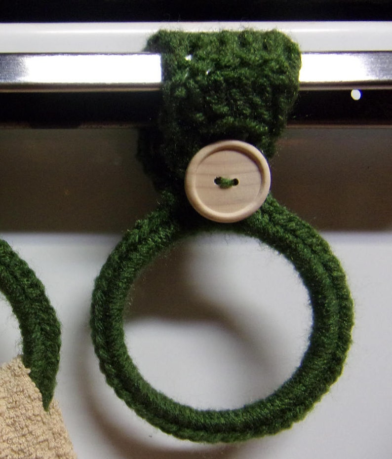 May include: Two green crocheted towel rings with wooden buttons. The rings are hanging on a metal bar.