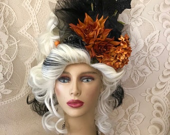 May include: A mannequin head with a white and black wig, adorned with a black and orange Halloween-themed headpiece. The headpiece features black tulle, orange flowers, and a bat silhouette. A sparkling rhinestone necklace completes the look.