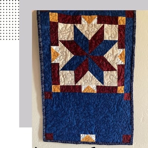 May include: A blue, red and yellow Americana Star quilt pattern placemat. The placemat is quilted with a swirling pattern and has a dark blue border.