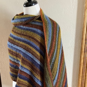 May include: A striped crocheted shawl in shades of brown, green, blue, and orange. The shawl is draped over a mannequin.