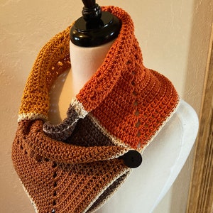May include: A crocheted cowl with a button closure. The cowl is made in shades of orange, brown, and white.