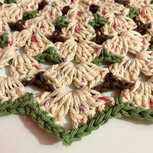 May include: A crocheted doily with a cream background and green, brown, and pink accents. The doily has a delicate, intricate design.