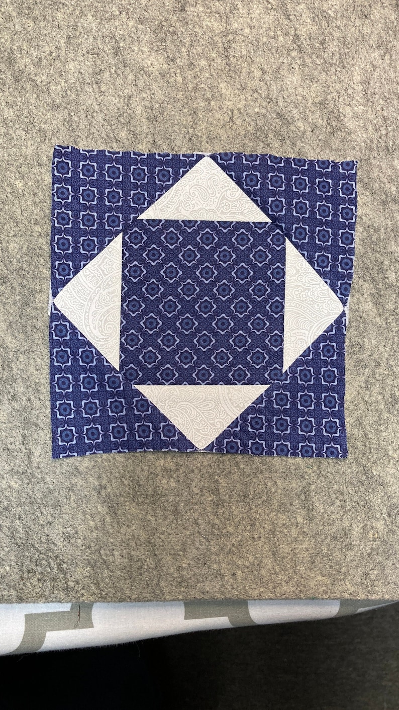 May include: A blue and white quilt block with a geometric design. The block is made of four white triangles and a blue square with a smaller white square in the center. The blue fabric has a small white floral pattern. Beginner Square in a Square Exploding Quilt Block Tutorial , Quilt Block Printable PDF, modern quilt block, easy quilt block pattern